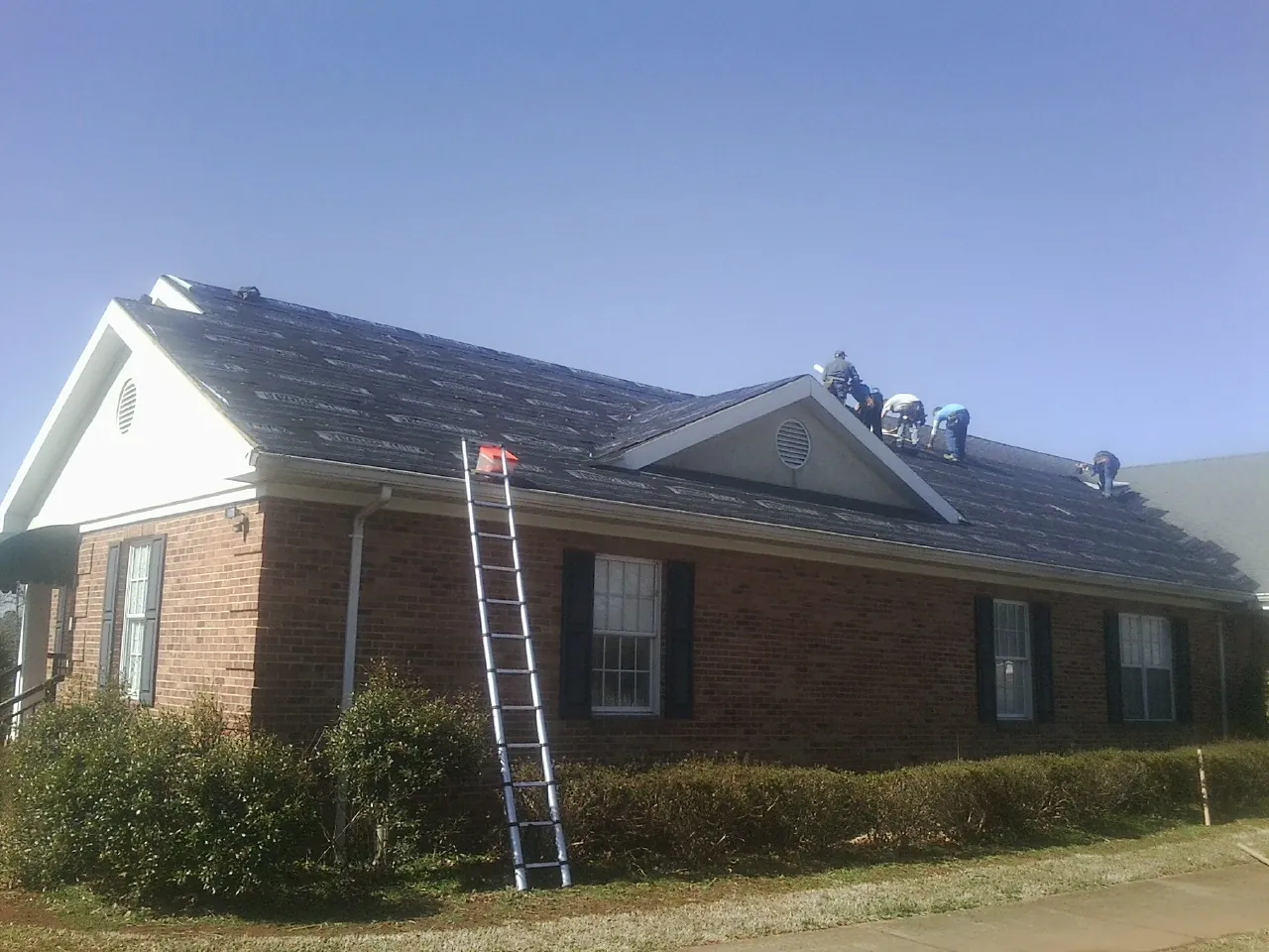 Crew tearing shingles off a brick ranch roof with a ladder set — Emergency Roof Repair work by our crew in Orinda