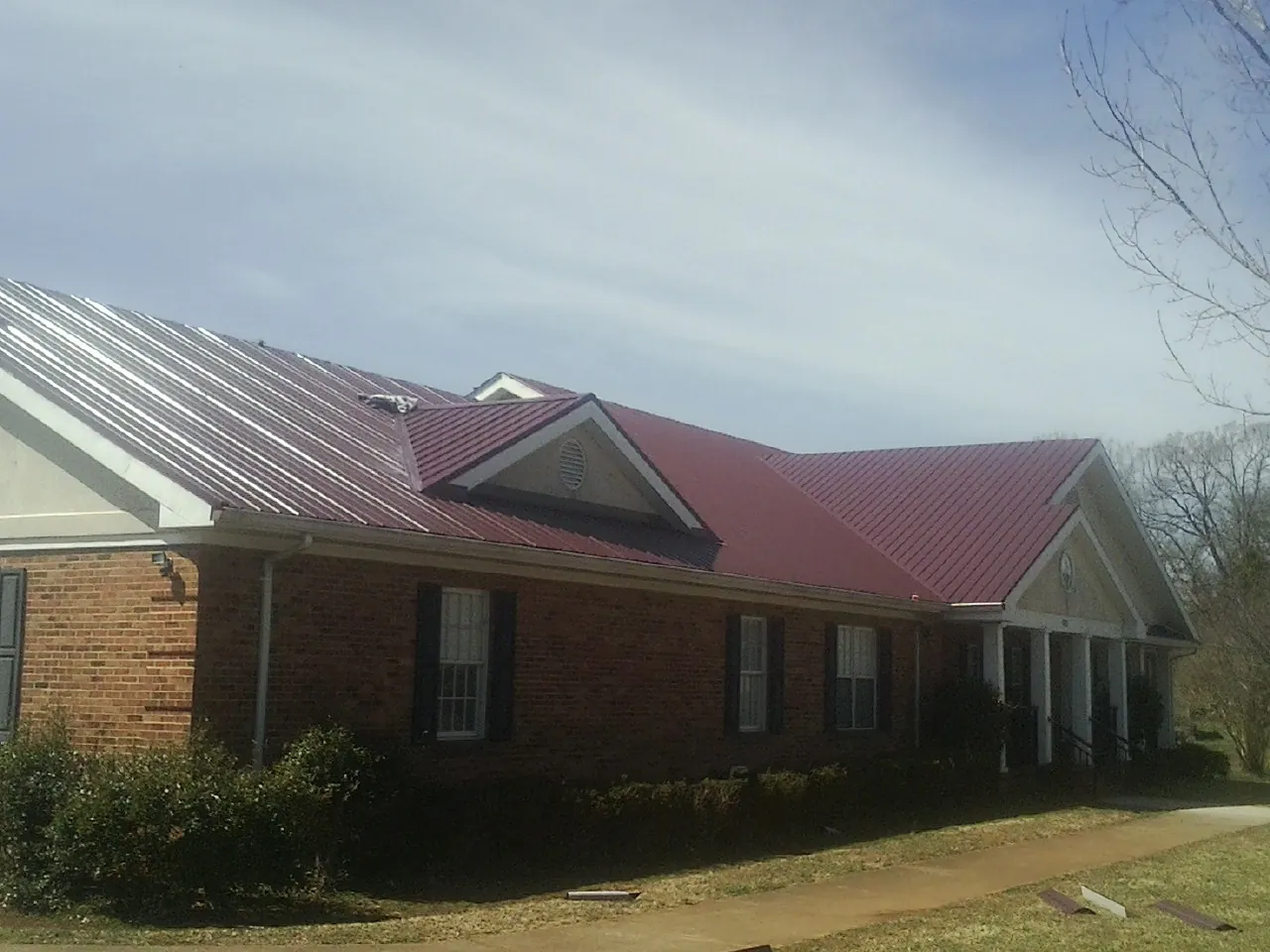 Red metal roof with gabled entries on a long brick building, from a Hail Damage Roof Repair job in Orinda