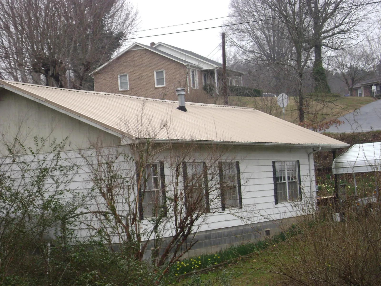 Tan metal roof on a white sided house set into a hillside — Commercial Roofing by Roofing Brothers in Orinda